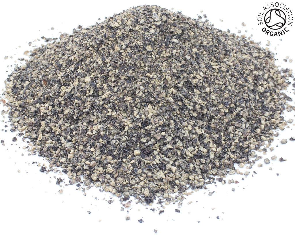 A small pile of organic cut cracked black pepper peppercorns on a white back ground with the Soil Association Organic Logo in the top right corner