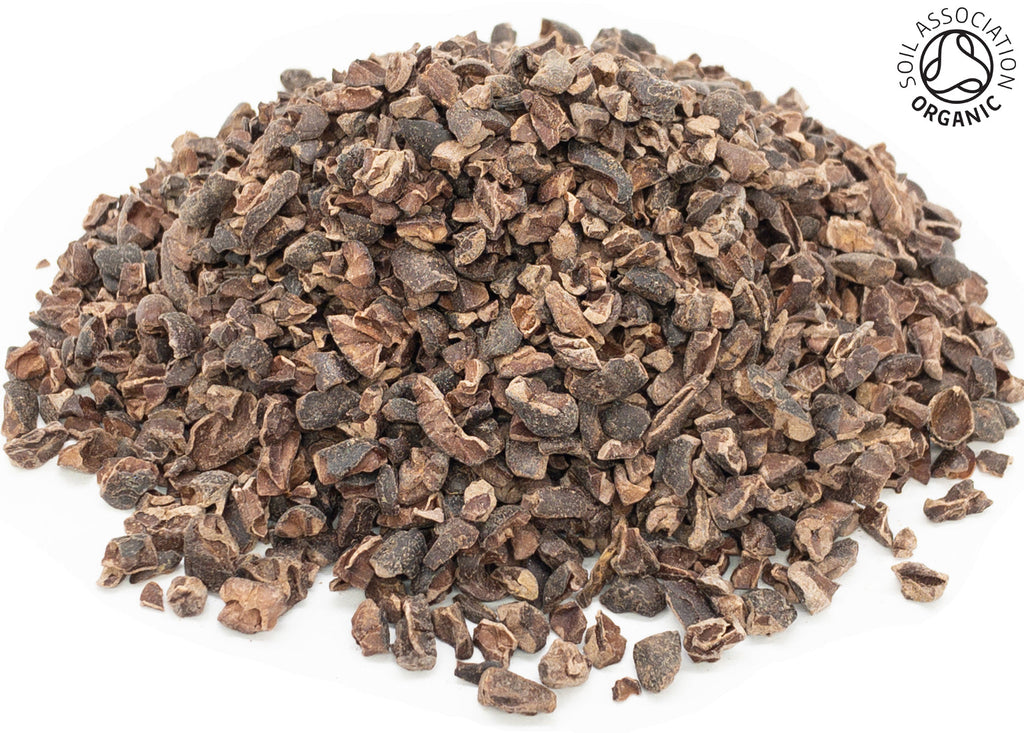A small pile of dried, cut, organic cacao nib pieces on a white background with the Soil Association Organic Logo in the top right corner
