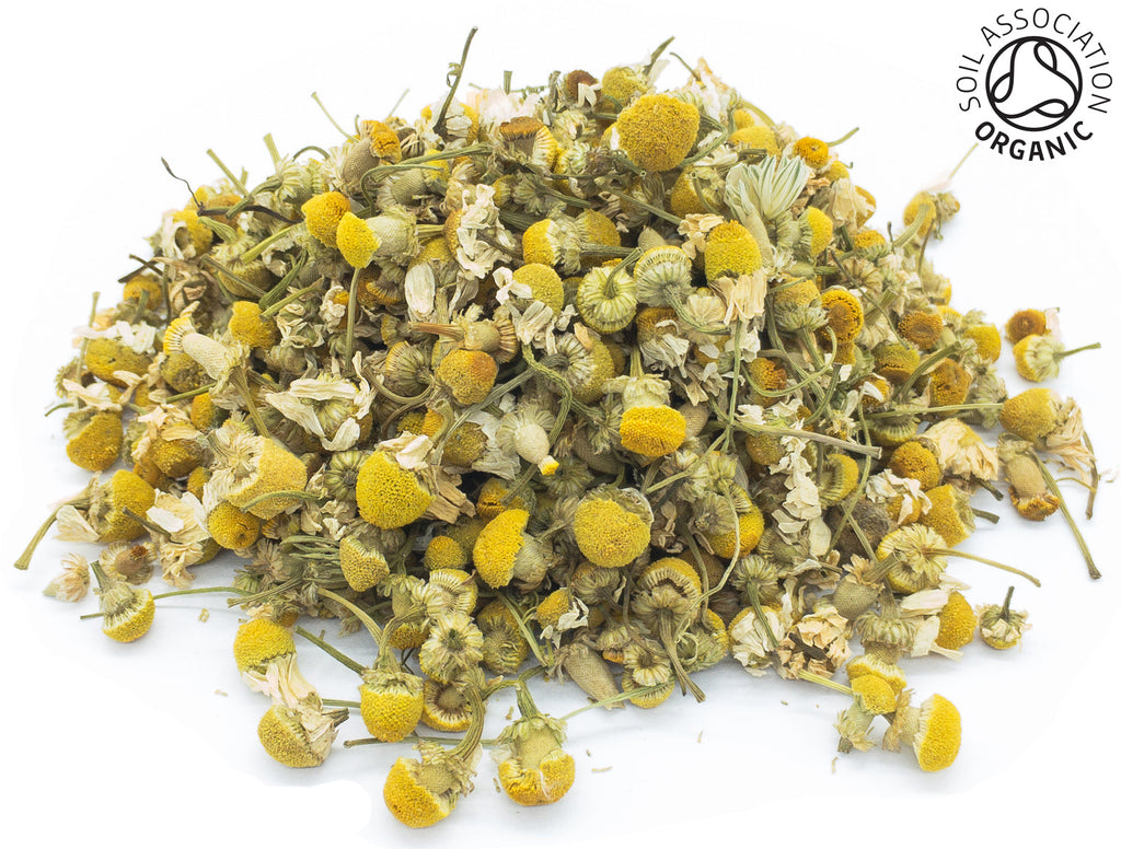 A small pile of dried, chamomile camomile flower buds on a white background with the Soil Association Organic Logo in the top right corner