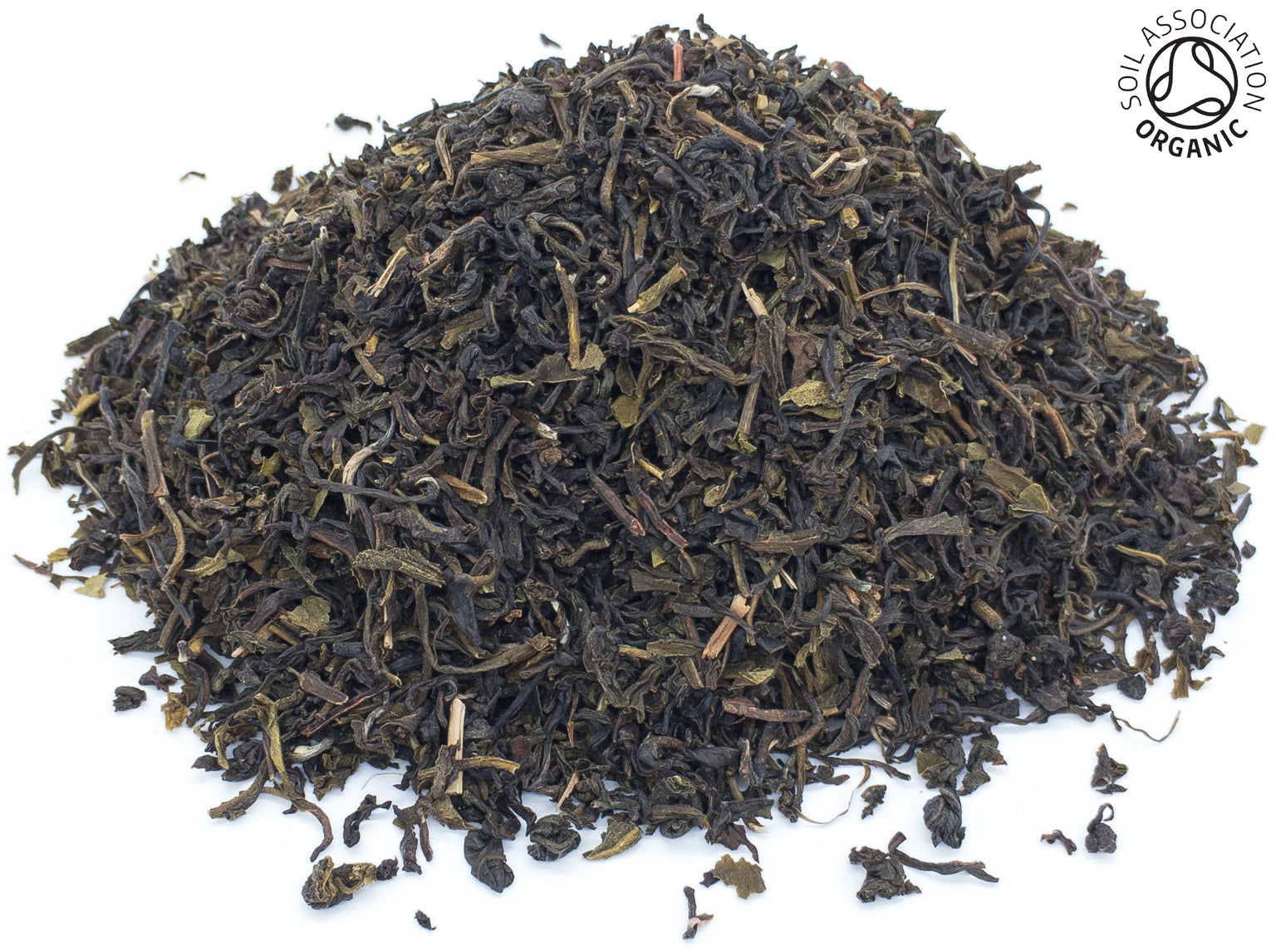 A small pile of dried, cut, organic green tea leaves from Dooars, India, on a white background with the Soil Association organic logo in the top right corner