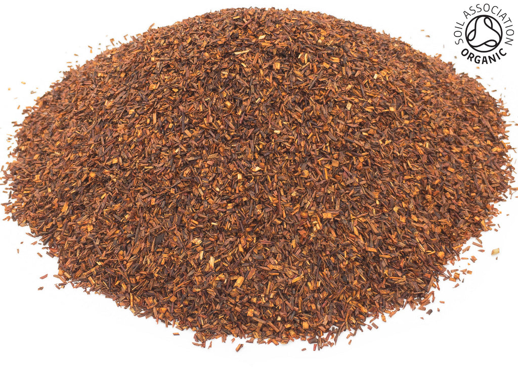 A small pile of cut red rooibos leaves, on a white background, with the Soil Association Organic logo in the top right hand corner